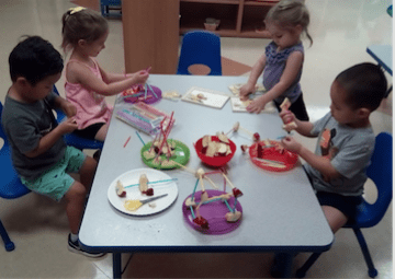 Four children building with fruit and straws.