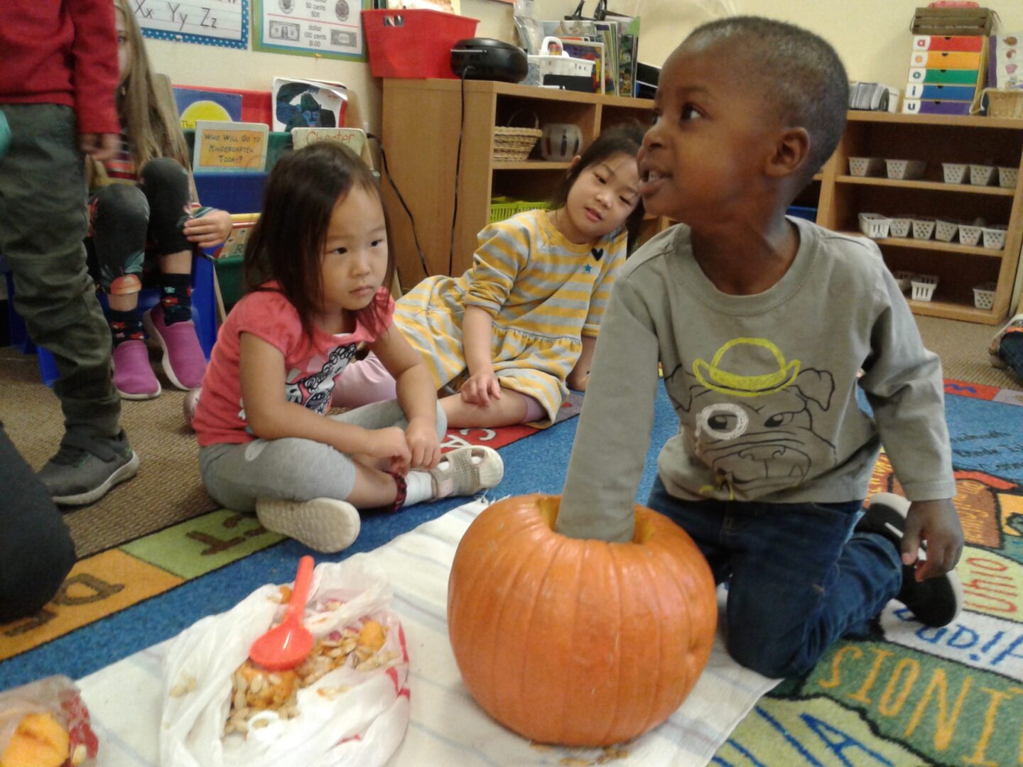 Young boy holding a pumpkin in a classroom.