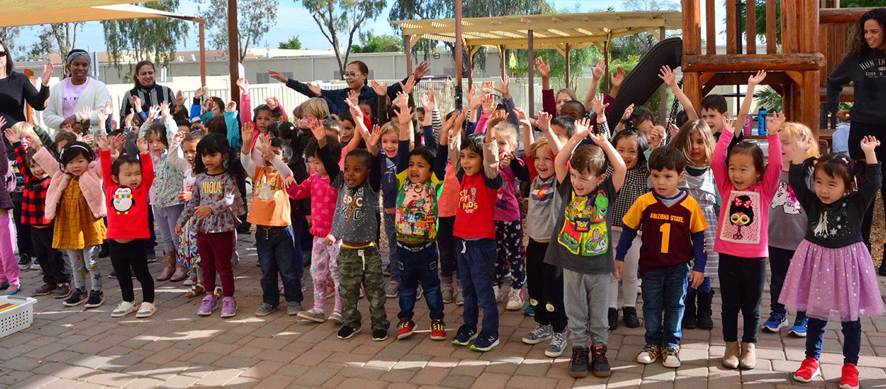 Large group of preschool children raising hands.