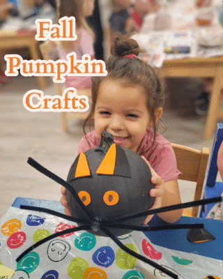 Photo of a toddler holding a pumpkin that is painted and decorated to look like a black cat.