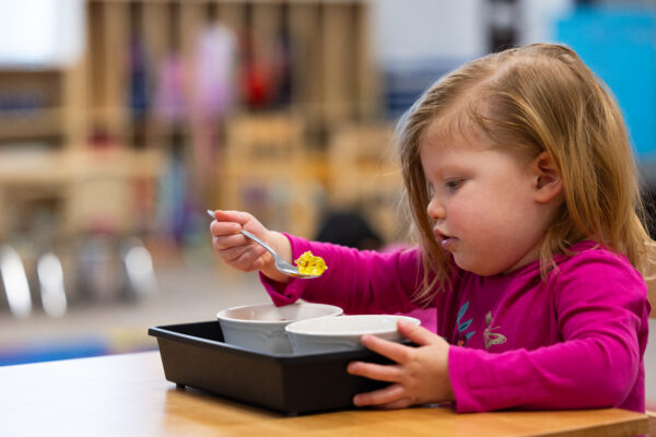 A girl is engaged in a Montessori Practical Life work where she is using a spoon to scoop beads between two bowls.