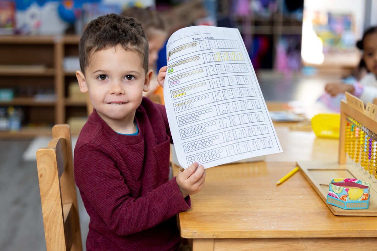 Child proudly showing completed Montessori classroom work at Inspire Kids Montessori